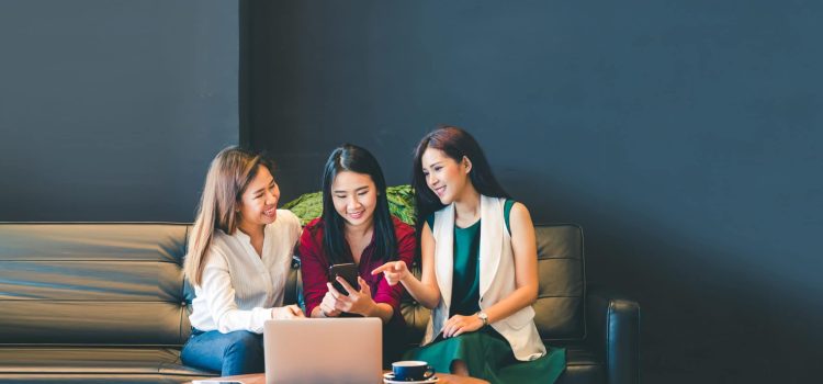 Three women look at a smartphone.
