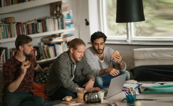 Three college students eating sandwiches while working on a group project