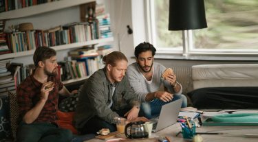 Three college students eating sandwiches while working on a group project