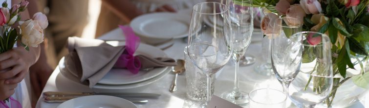 A close-up image of a table at a wedding reception with pink roses, wine, champagne glasses, and plates.