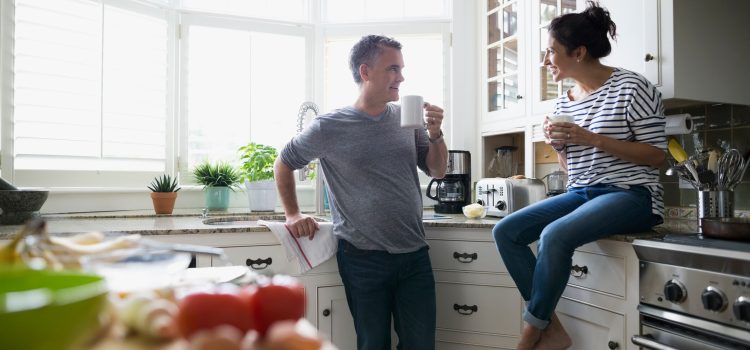 Husband and wife talking in their kitchen while enjoying a cup of coffee.