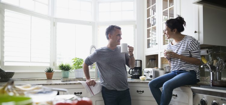Husband and wife talking in their kitchen while enjoying a cup of coffee.