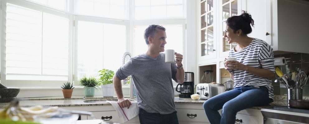 Husband and wife talking in their kitchen while enjoying a cup of coffee.