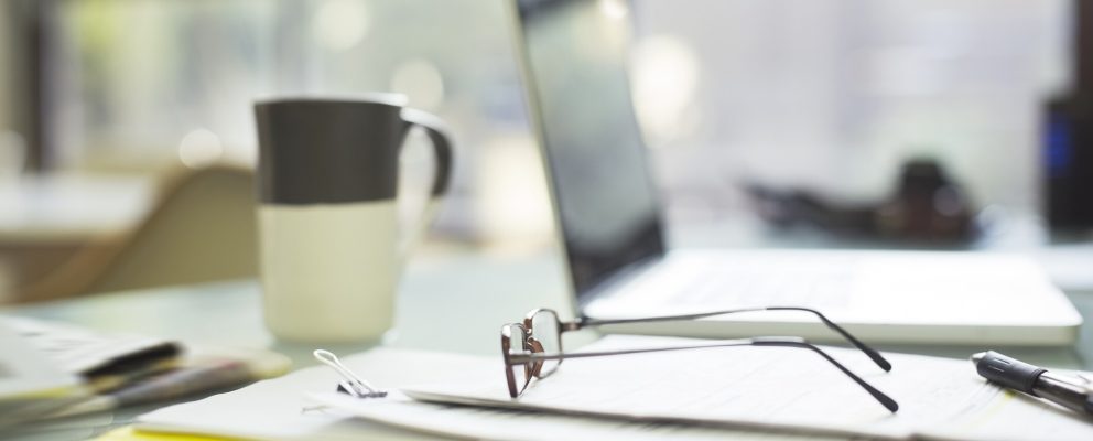 Financial papers, reading glasses, and laptop strewn about desk