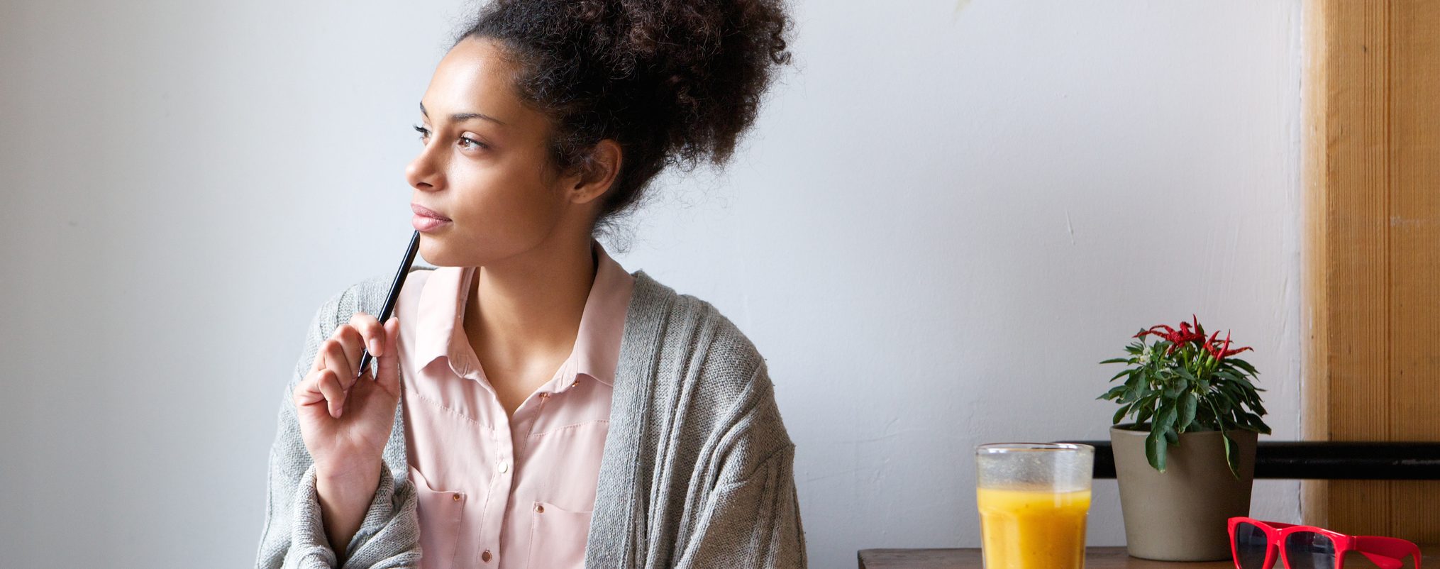 A woman holding a pen, sitting at a desk and contemplating.