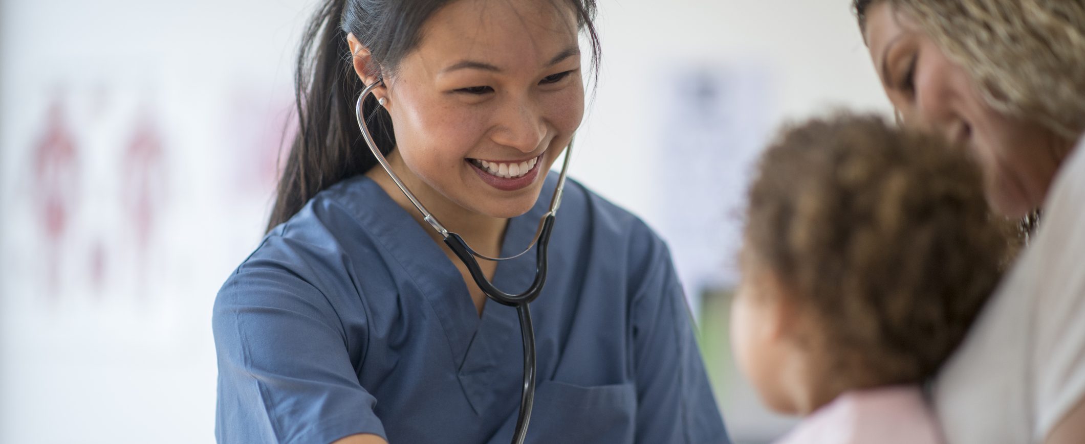 A smiling pediatrician meeting with a young patient and her mother.