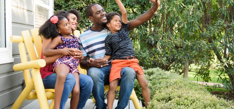 A mother and father with their son and daughter sitting on a bench outside.
