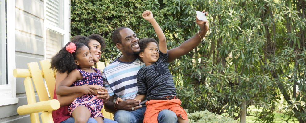 A mother and father with their son and daughter sitting on a bench outside.