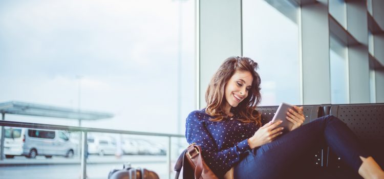 A woman sits on a bench and reviews her bank account on her tablet.