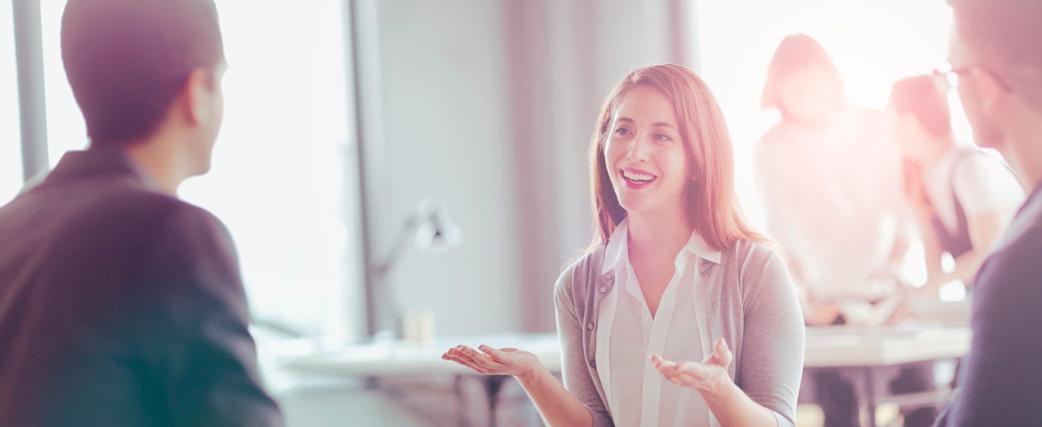 A woman talks with two coworkers while motioning with her hands.