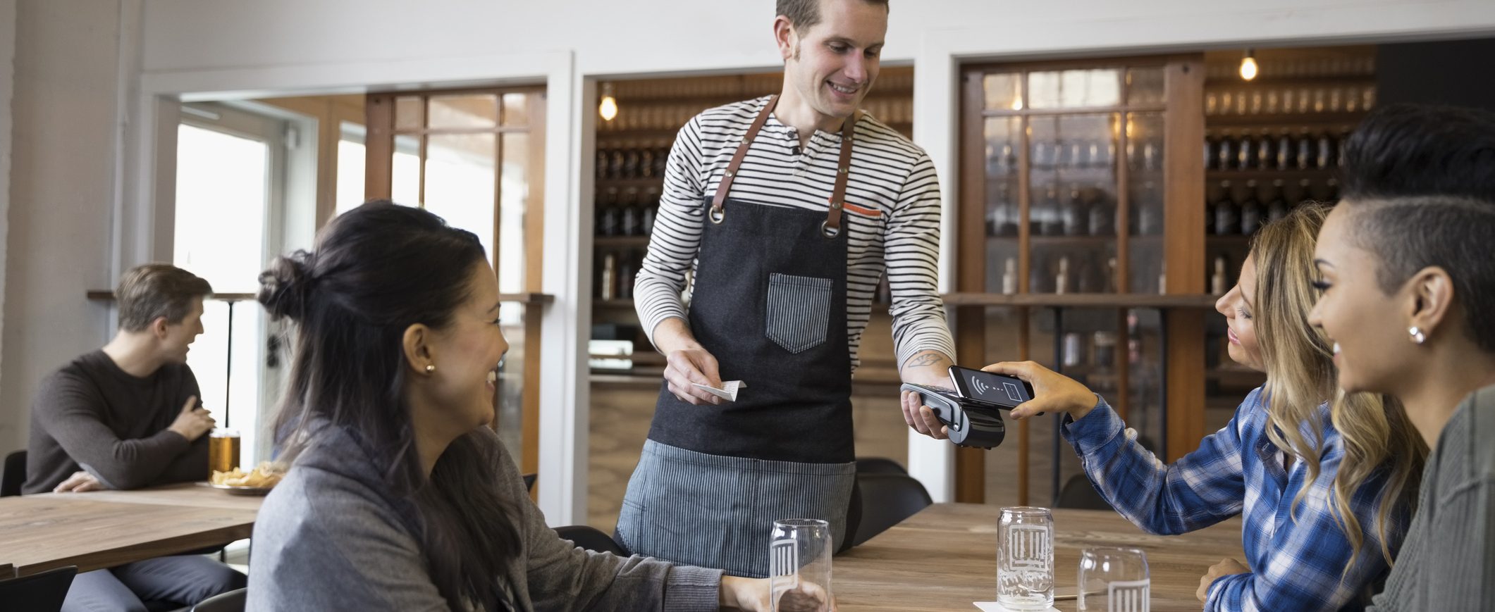 A woman uses her mobile device to pay a waiter at a restaurant.