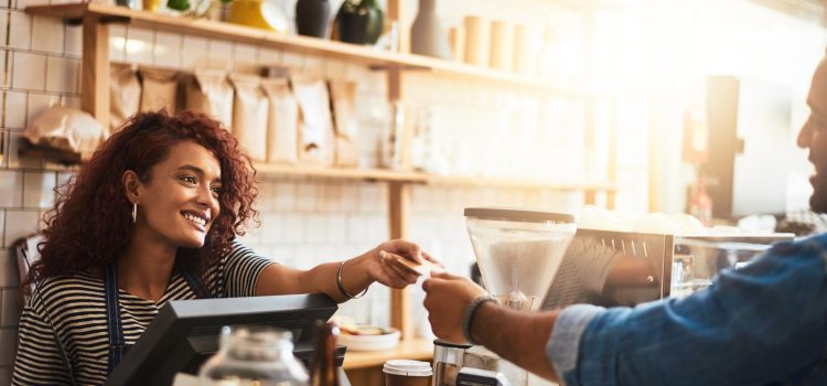 Woman smiling and handing her payment card to the cashier at a coffee shop.