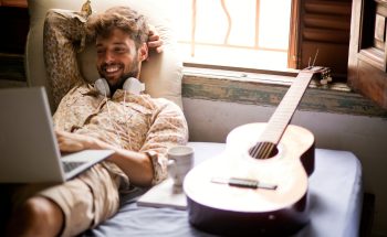 Man with headphones around his neck smiling at his computer.