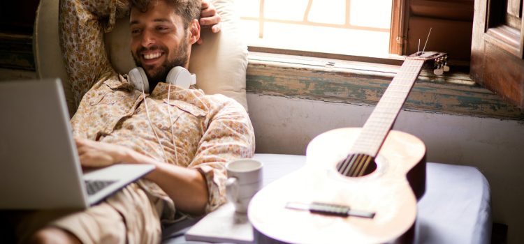 Man with headphones around his neck smiling at his computer.