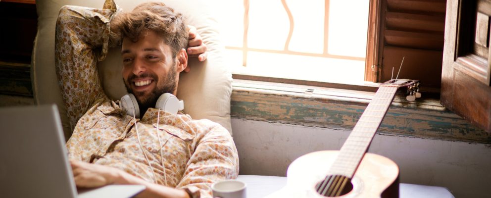 Man with headphones around his neck smiling at his computer.