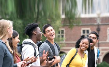 A group of college students laughing outside a campus building.