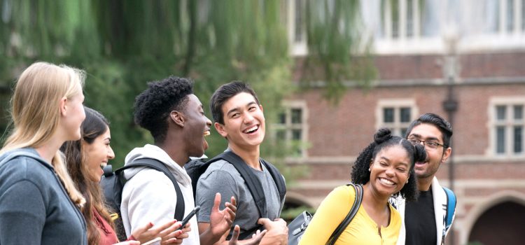 A group of college students laughing outside a campus building.