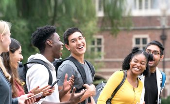 A group of college students laughing outside a campus building.