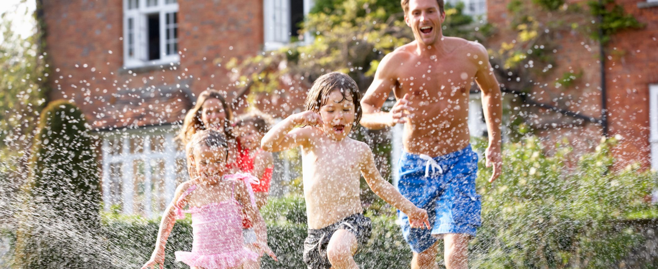 A family runs through a sprinkler in a backyard.