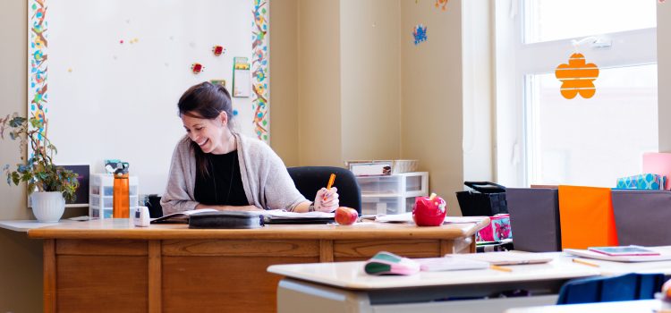 A teacher sits at her desk at school and looks over papers.