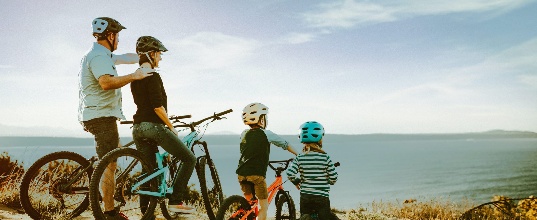 A family of four, out for a bike ride, gazes out at the ocean as they take a break.