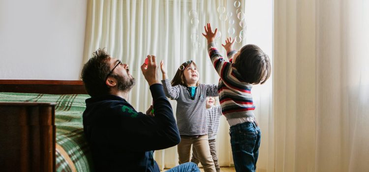 A dad blows bubbles while playing with his 2 kids