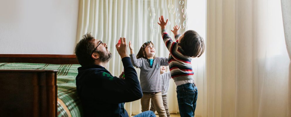 A dad blows bubbles while playing with his 2 kids