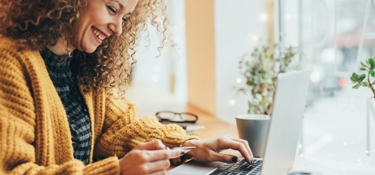 A close up of a woman reading her credit card to input the card number on her laptop keyboard.