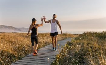 A man and a woman in workout gear high five in a field by the ocean.