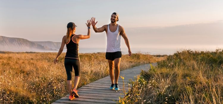 A man and a woman in workout gear high five in a field by the ocean.