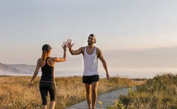 A man and a woman in workout gear high five in a field by the ocean.