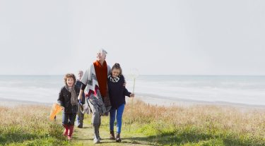 A young girl and boy walking with their grandma on the beach.