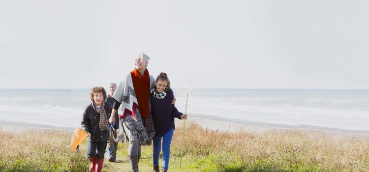 A young girl and boy walking with their grandma on the beach.