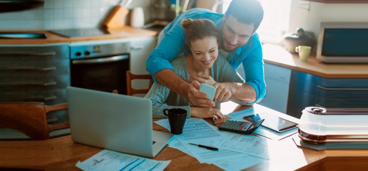Couple looking at a mobile phone while reviewing paperwork in their kitchen