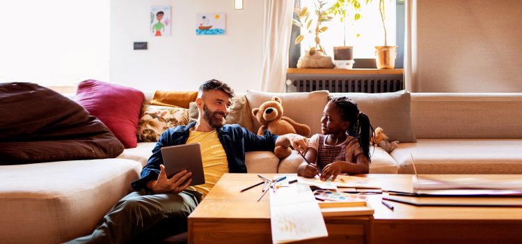 A man smiles at his daughter while she draws