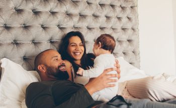 A couple holds their baby in bed.