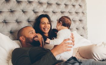 A couple lies in bed and smiles at their baby