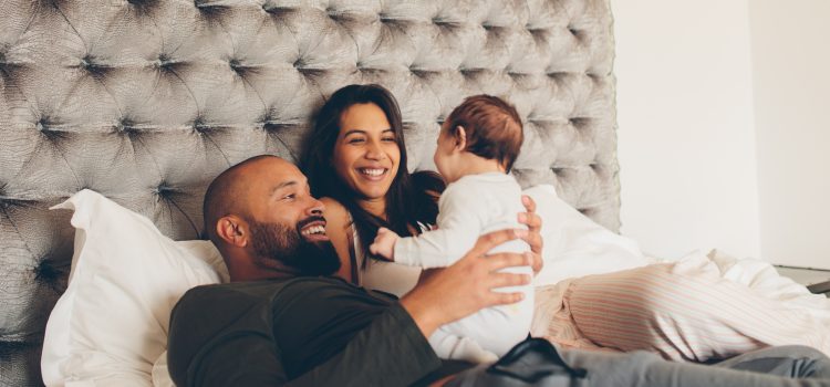 A couple lies in bed and smiles at their baby