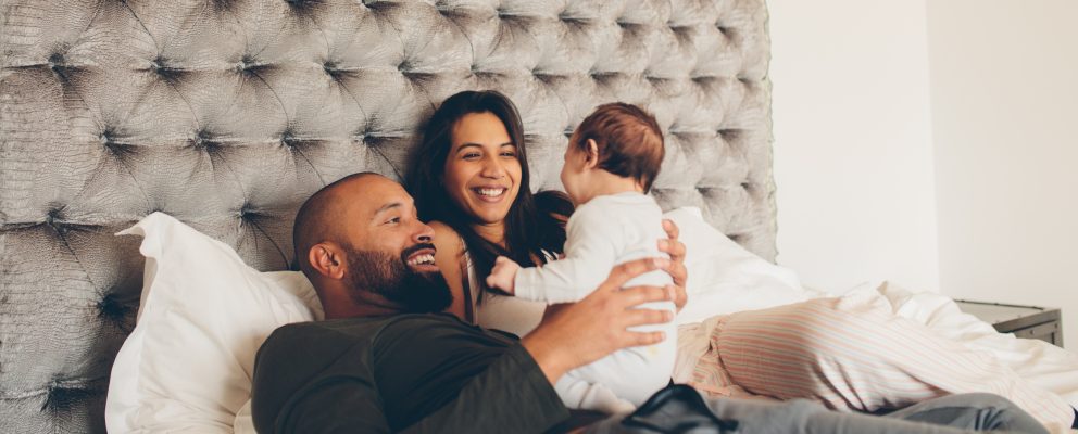 A couple lies in bed and smiles at their baby