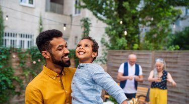 A father holds his son and smiles as they look up to the sky