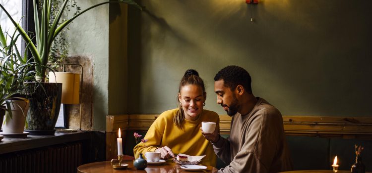 A couple at a café share a desert and drink coffee.