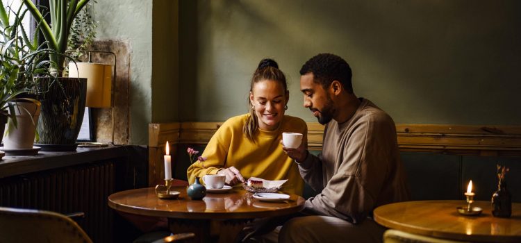 A couple at a café share a desert and drink coffee.