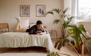 Woman writing in a journal while laying on her bed.