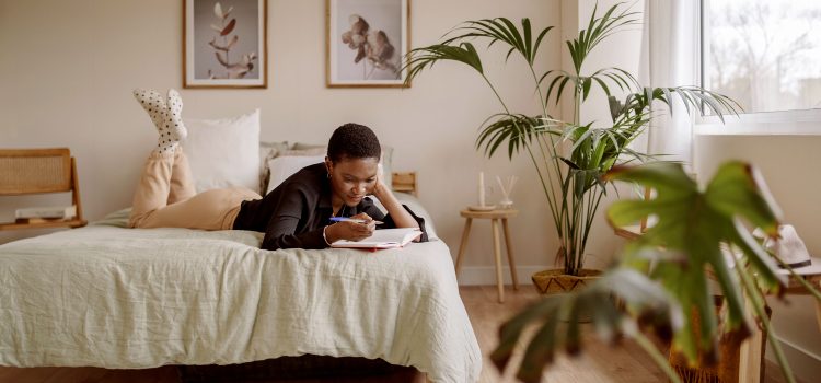 Woman writing in a journal while laying on her bed.