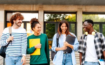 Four college students are walking and smiling holding their books