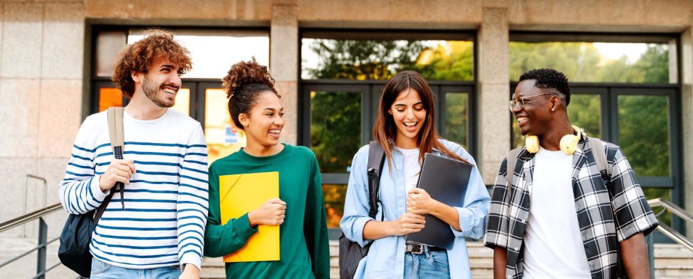 Four college students are walking and smiling holding their books