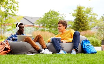 Two college students sit on bean bag chairs in the grass