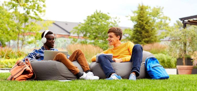 Two college students sit on bean bag chairs in the grass
