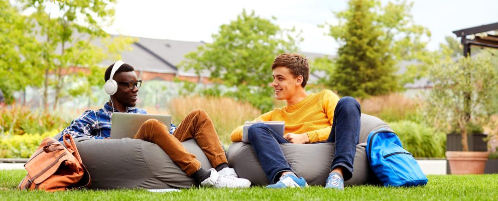Two college students sit on bean bag chairs in the grass