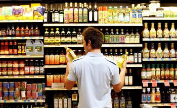 A man stands in front of a grocery store aisle and compares bottles in each hand